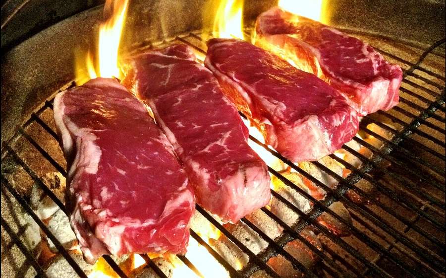 Thick steaks searing over open flames on a hot grill grate