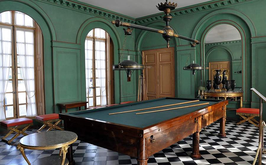 Billiard table in a bright room with tall arched garden windows (representative photo)