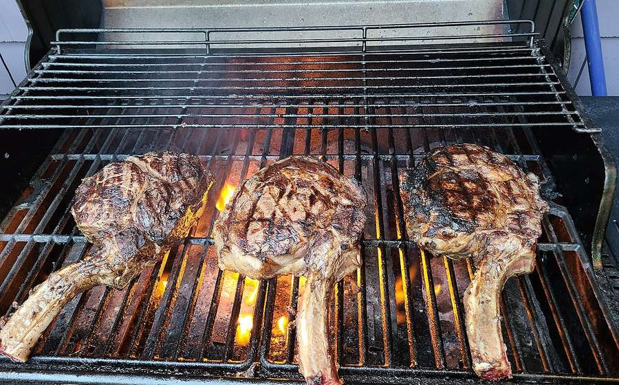 Tomahawk steaks searing over flames on a grill